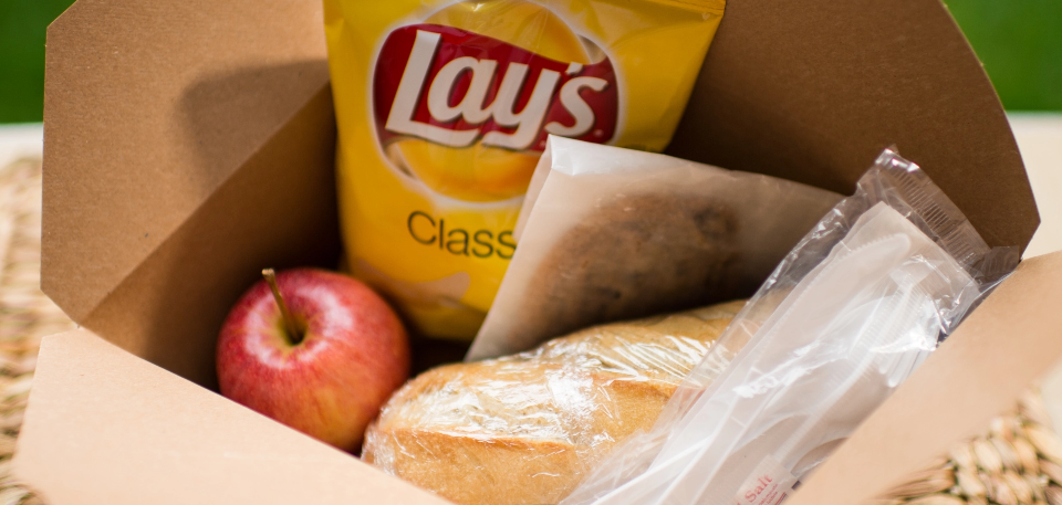 Boxed lunch containing a sandwich, potato chips, apple and cookie