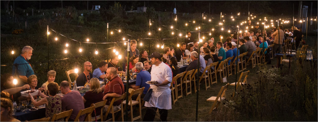 A night scene A long table filled with people sharing a meal illuminated by cafe lights