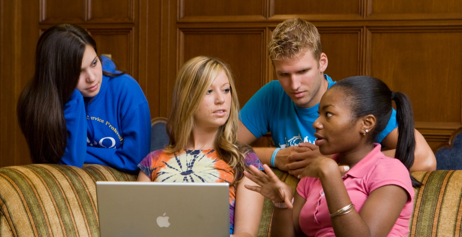 Four students having a disscussion while looking at a laptop