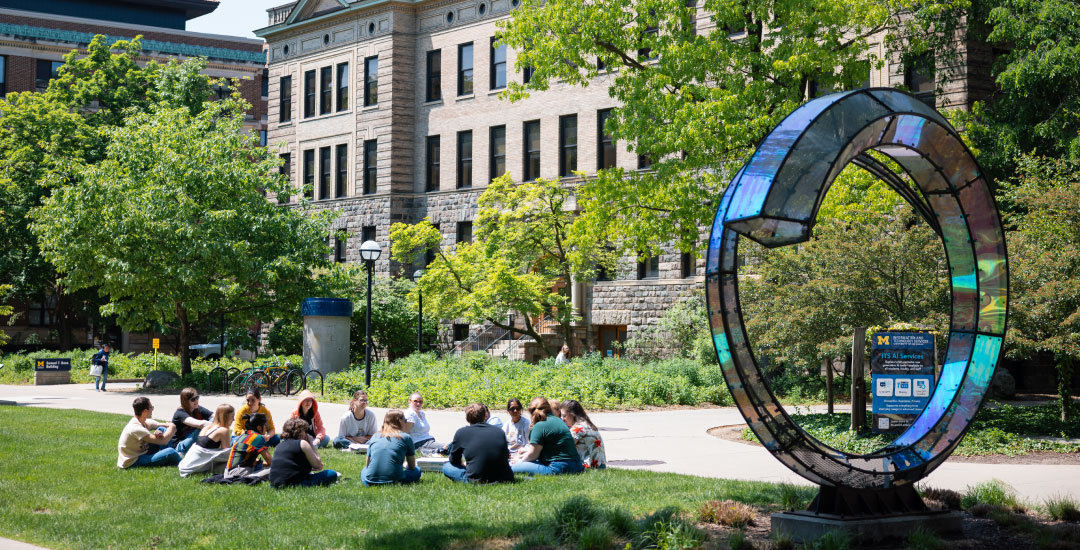 Group of students sitting in a circle on the grass outside of Samuel T. Dana Building
